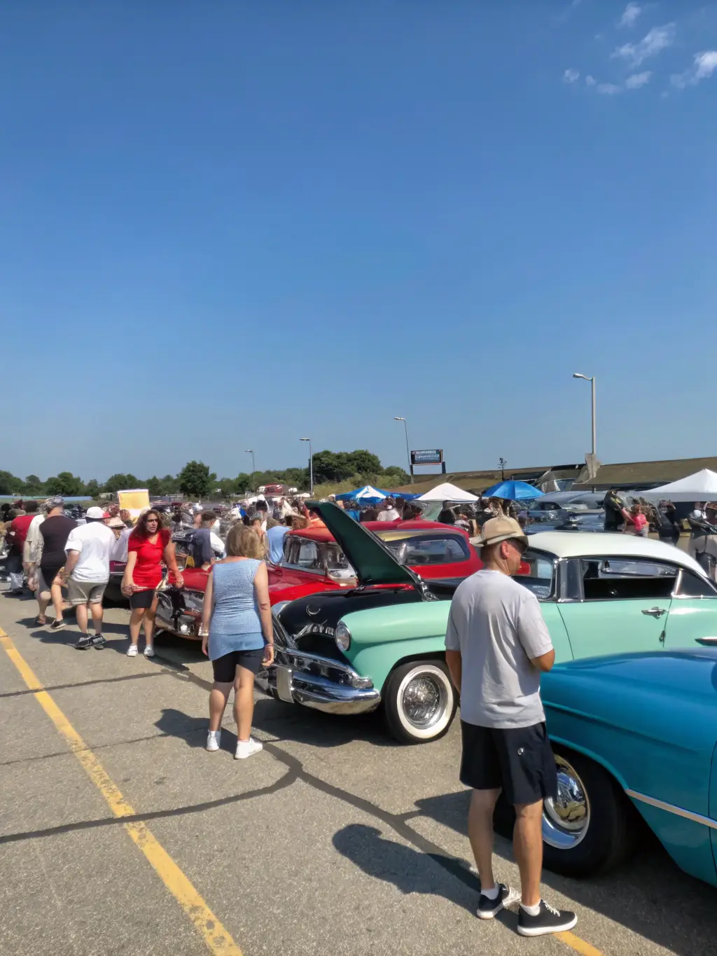 A picture of club members participating in a car show, displaying their vehicles and interacting with the public.